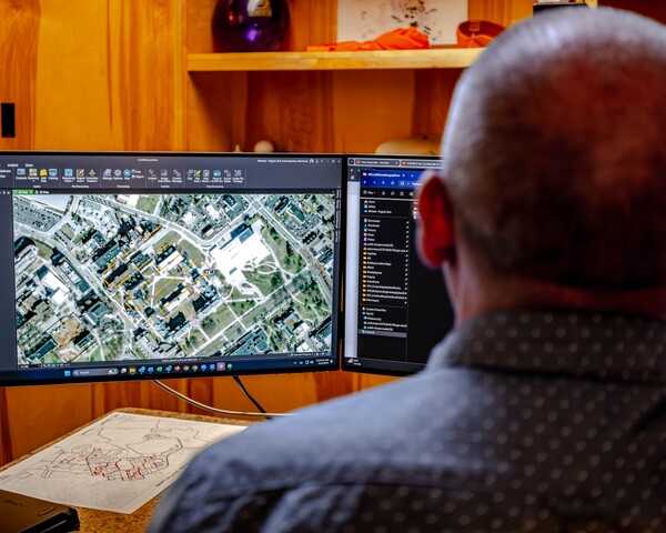 Man views aerial campus maps on multiple monitors in an office.