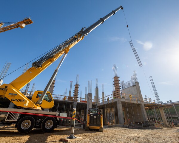 Yellow crane puts a rebar cage in place on a large construction site. 