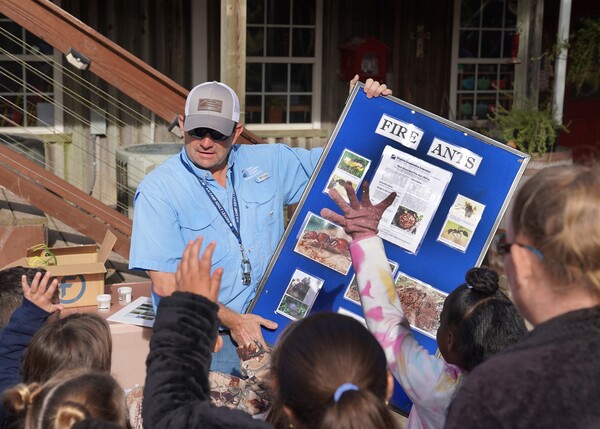A man holds a posterboard with information about fire ants to a group of children.
