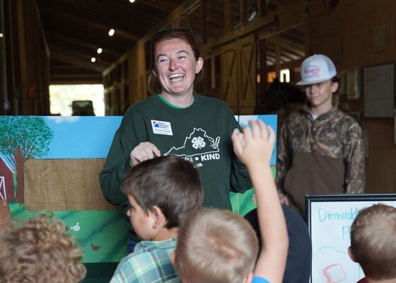 A woman smiling standing in a barn while presenting to children about farms.
