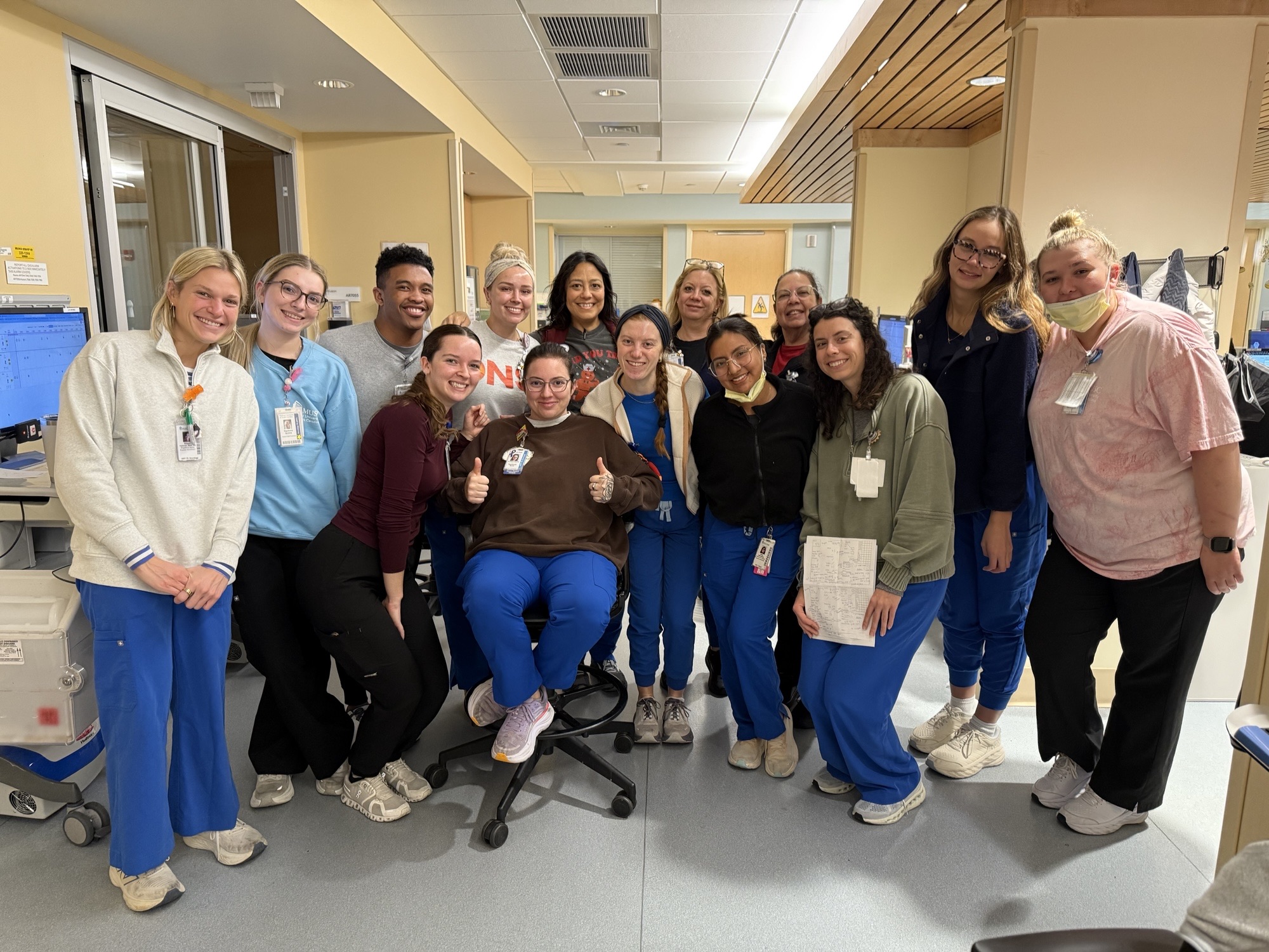 Four nurses dressed in navy scrubs examine a patient chart together.