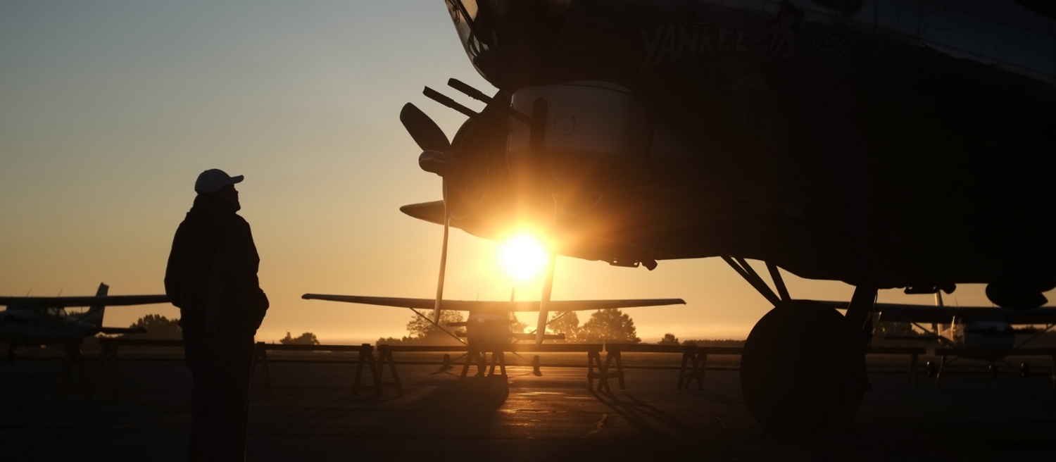 A Kent State employee looking proudly at an airplane, the sun setting in the background.