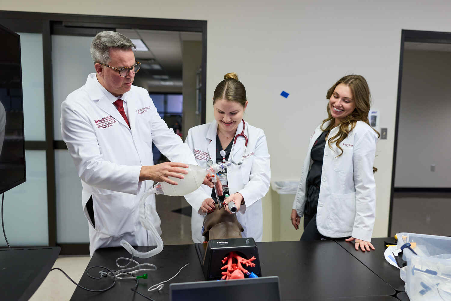 People in white lab coats gather around a table examining an anatomical model.