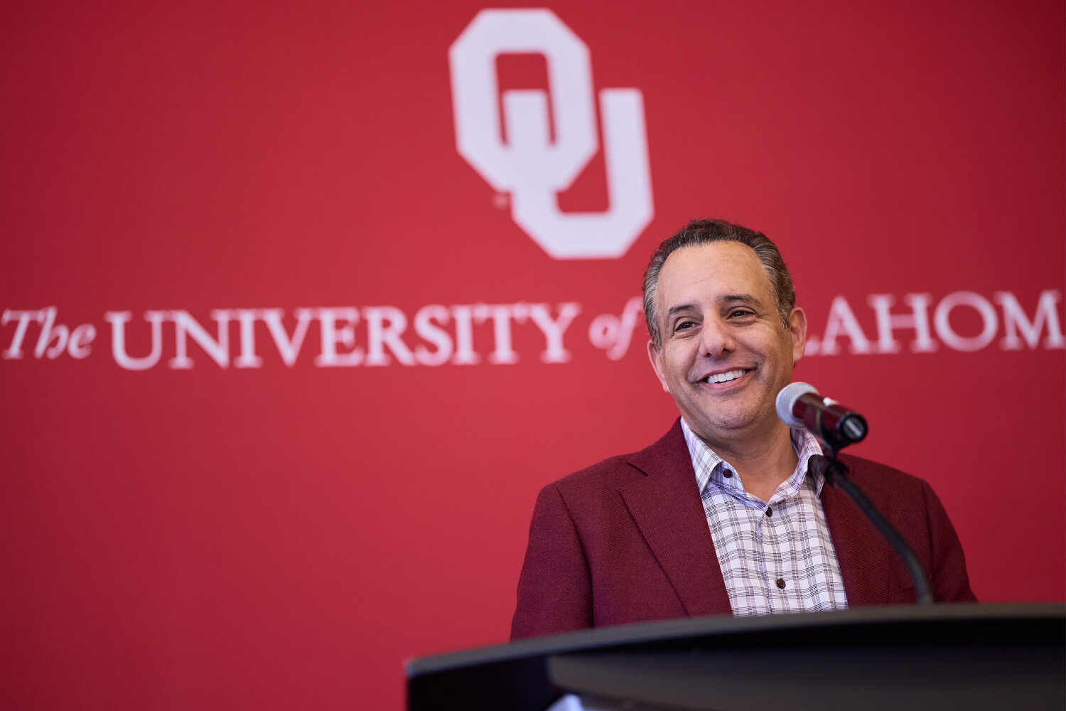 President Joseph Harroz Jr. stands at a podium in front of a red backdrop with the OU logo and “University of Oklahoma.”