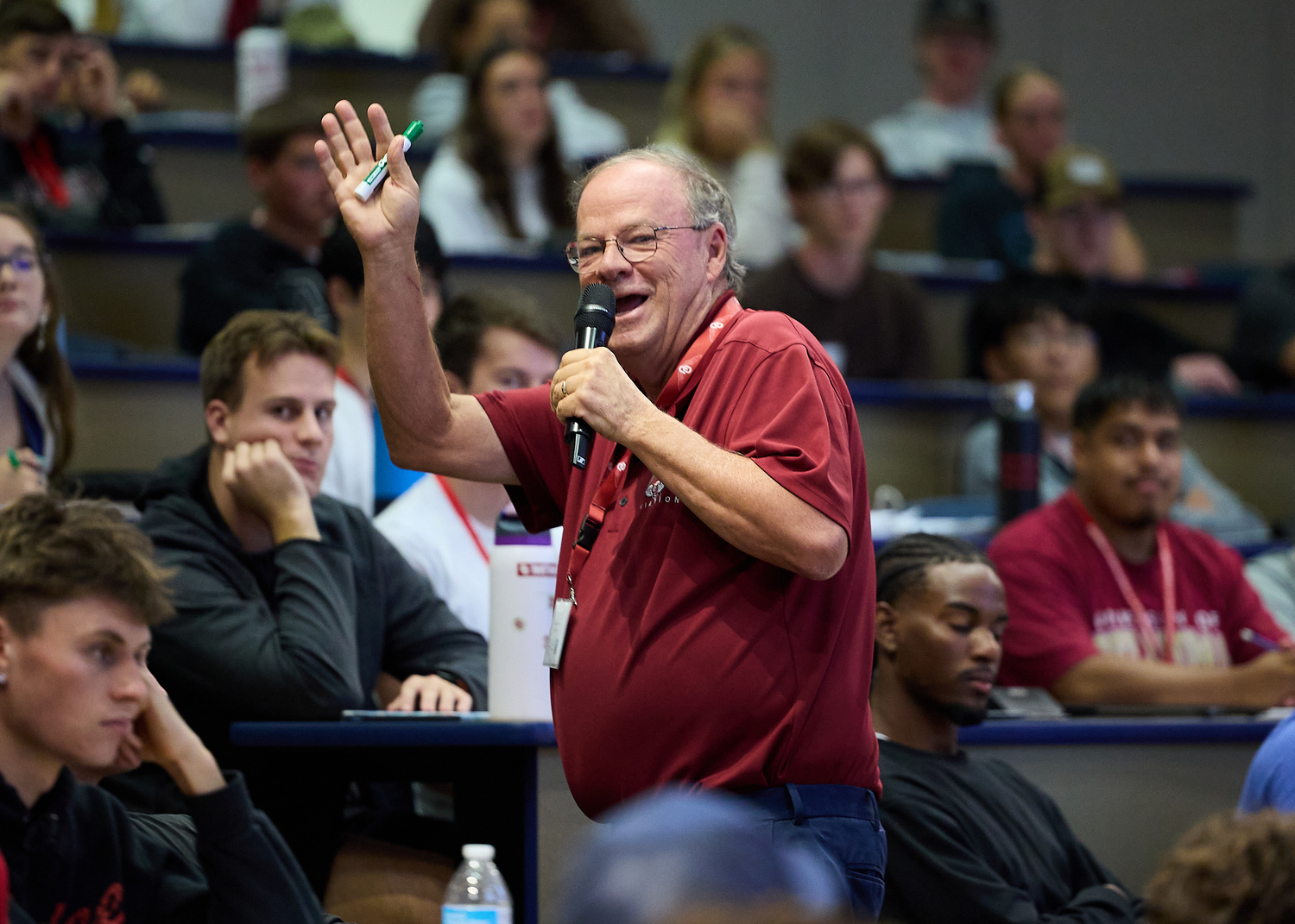 A person speaks into a microphone while raising a hand in front of an audience.